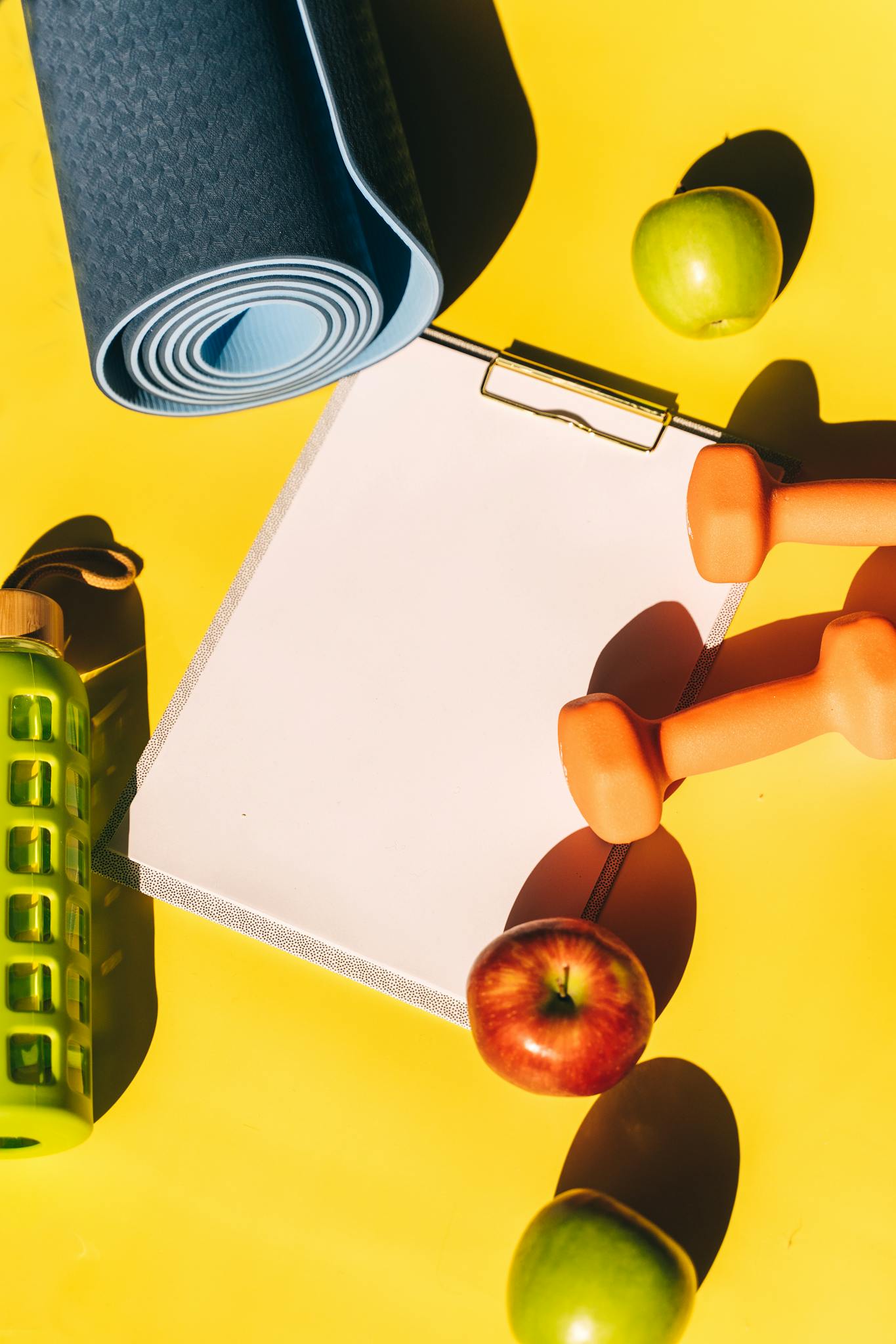 A flat lay of fitness equipment, fruits, and a clipboard on a vibrant yellow background.