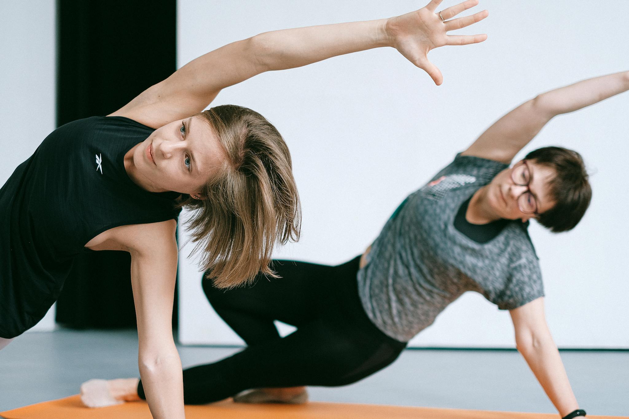 Two women engaging in yoga exercises on an orange mat in a studio setting.