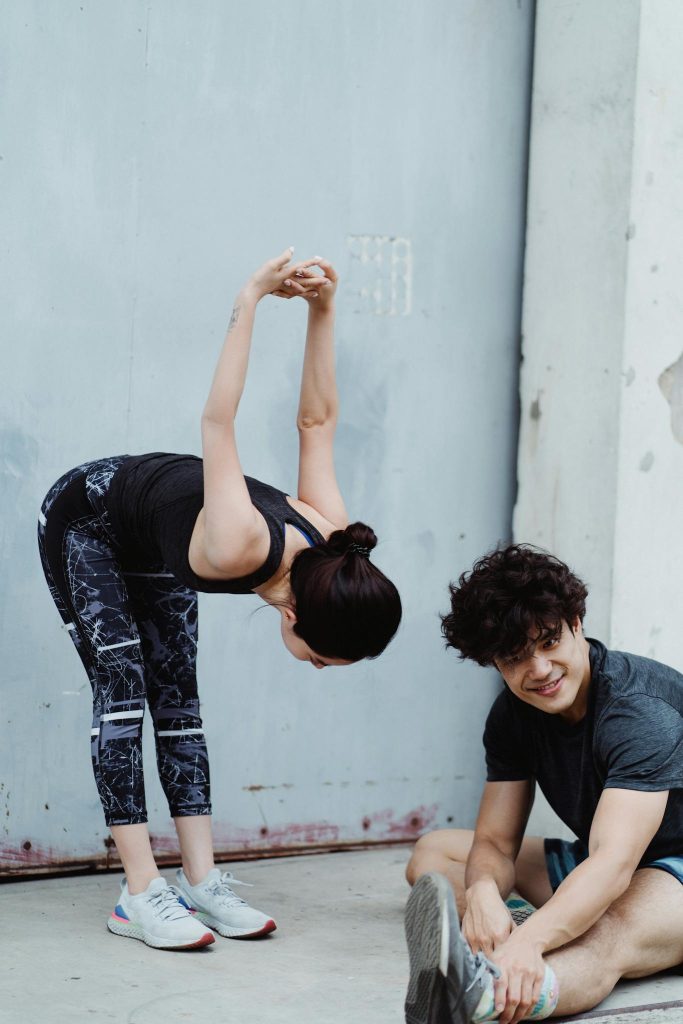 Two young adults stretching in sportswear during an outdoor workout session.