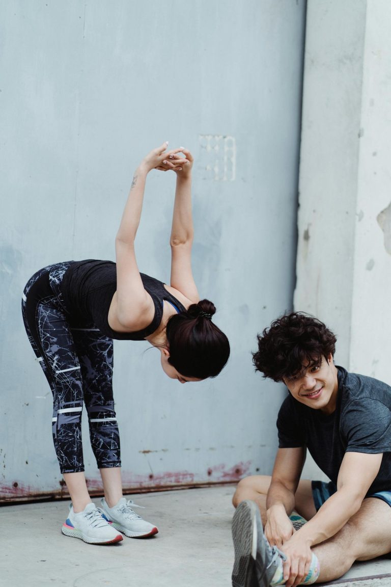 Two young adults stretching in sportswear during an outdoor workout session.
